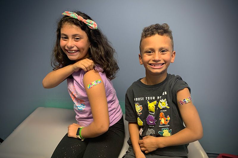 two children proudly showing off their band-aids after receiving vaccinations