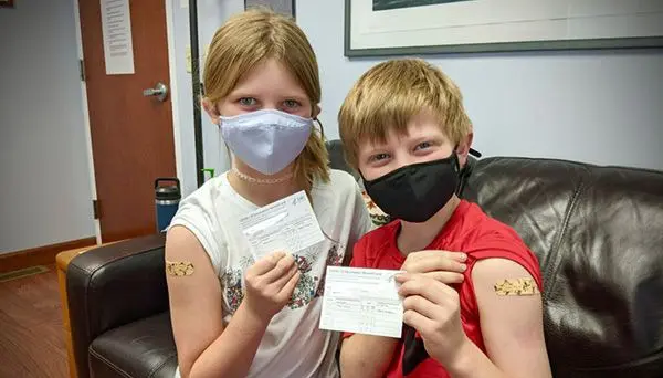 two children proudly showing off their band-aids and vaccination cards