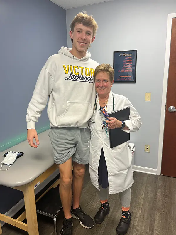 A tall teenager stands smiling next to Dr. Casey. They are both in an office with blue walls and a treatment table.