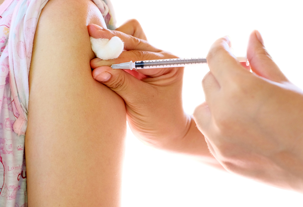 A person receives an injection in the upper arm, with one hand holding a cotton ball near the injection site and the other hand administering the shot with a syringe.
